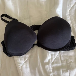 Svart Pusch up bh med justerbara axelband - Säljer en klassisk svart Pusch up bh med justerbara axelband och hakknäppning bak. Den har en slät design och ger bra stöd. Perfekt för vardagsbruk eller under festkläder. Sparsamt använd. Vet ej storlek gissar på 75A eller B. Aningen bucklig på höger kupa annars bra skick 
