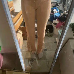 Korall byxor från Juicy Couture - Säljer ett par snygga korall byxor från Juicy Couture. Byxorna har en hög midja och raka ben, vilket ger en stilren look. Perfekta för en avslappnad men chic stil.