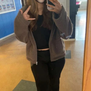 Brun teddyjacka med dragkedja - Mysig brun teddyjacka med dragkedja framtill. Perfekt för kyliga dagar och ger en avslappnad look. Jackan har långa ärmar och en bekväm passform.