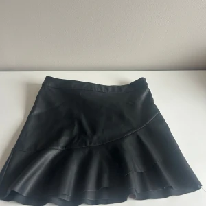 Svart kjol med volangdetalj - Snygg svart kjol med volanger i skin som passar bra till sommaren men även vintern med ett par strumpbyxor🥰 tryck gärna på köp nu🥰 jag kan tyvärr inte andvända den längre eftersom att den är för liten💗💗