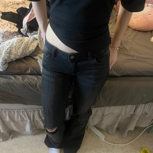 Svarta jeans med slitdetalj - Snygga svarta jeans med en liten slitdetalj vid knät. De har en klassisk femficksdesign och en knappgylf. Perfekta för en avslappnad stil.