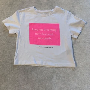 Vit t-shirt med rosa tryck - Säljer en vit t-shirt från H&M med ett stort rosa tryck på framsidan med texten 'keep on dreaming new days and new goals'. Perfekt för en avslappnad stil. Kortärmad och i bomullsmaterial.
