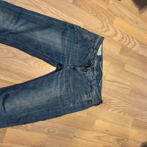 Dondup George 28/30 - Snygga blå jeans med en klassisk femficksdesign och subtila slitningar för en trendig look. De har en knappgylf, vilket gör dem perfekta för en avslappnad stil.