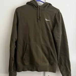 Olivgrön hoodie från Nike - Säljer en olivgrön hoodie från Nike med en klassisk känguruficka och justerbar huva. Den har en liten vit Nike-logga på bröstet. Perfekt för en avslappnad stil.