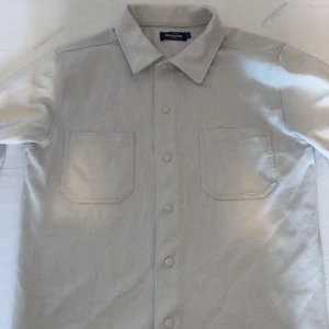 Vit dressmann overshirt - Säljer en vit overshirt från dressmann. Overshirten har två bröstfickor och knappar framtill. Perfekt för en avslappnad stil.