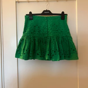 Grön kjol från Zara - Snygg grön kjol från Zara med broderade detaljer och volang. Kjolen har en kort längd och knappar framtill. Perfekt för att ge en färgklick till din outfit! Funkar för de som har s och även xs!