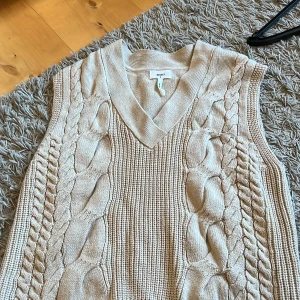Beige stickad väst från Object - Säljer en snygg beige stickad väst från Object med flätstickat mönster och v-ringning. Perfekt för lager-på-lager-stil och passar till många olika outfits. Ett måste i garderoben för den stilmedvetna! Pris diskuterbart!