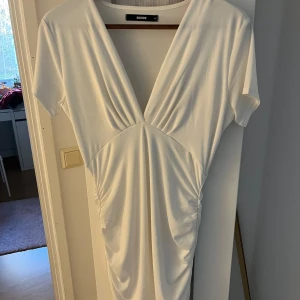 Vit klänning från Bubbleroom - Elegant vit klänning från Bik bok med v-ringad design och korta ärmar. Klänningen har en smickrande drapering framtill som ger en fin passform. Perfekt för sommarens tillställningar.