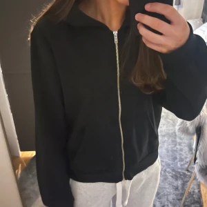 Svart zip-hoodie från Lager 157 - Säljer en klassisk svart hoodie med dragkedja framtill. Den har en bekväm passform och en praktisk huva. Perfekt för en avslappnad stil.