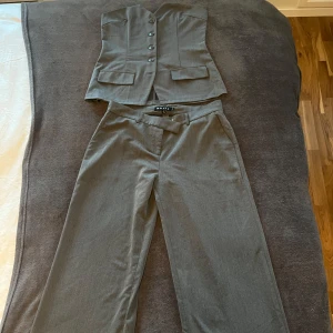 Grå kostym-set från motelrocks - Snygg grå väst från Motel med knappar framtill och två fickor och Lågmidjade kostymbyxor, Perfekt för en stilren look. Storlek M i både topp och byxa. Normal i strl men passar också en S. tyvärr för stor för mig därav säljer jag. Toppen är helt oanvänd och byxorna är använda fåtal gånger. 