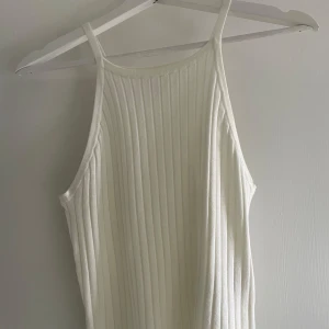 Vit ribbad linnetopp från H&M Divided - Säljer en stilren vit ribbad linnetopp från H&M Divided. Toppen har smala axelband och en enkel design som passar perfekt till sommaren. Perfekt för en avslappnad look eller att styla upp med accessoarer.