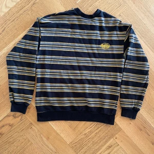 Randig tröja från Junkyard - Säljer en gul, svart och grå- randig tröja från Junkyard. Tröjan har långa ärmar och en rund halsringning.