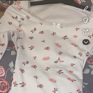 Vit blommig topp med spetsdetaljer - Söt vit topp med rosa blommönster och spetsdetaljer vid halsringningen. Den är från temu köpte för 119 men säljer för 75 väldigt bra skick. Säljer för 55 pris går att diskutera skriv för fler bilder. Xs men sitter lite löst skulle jag säga  