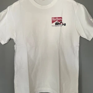 Vit t-shirt med Marlboro-tryck - Säljer en vit t-shirt med Marlboro World Championship Team-tryck. T-shirten har ett coolt motiv av en formel 1-bil både fram och bak. Perfekt för racingfans! 🏎️