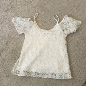 Vit spetsblus från Gina Tricot - Säljer en söt vit spetsblus från Gina Tricot i storlek XS. Blusen har korta ärmar och smala axelband, perfekt för en somrig look. Den är tillverkad i ett vackert spetsmaterial som ger en romantisk känsla. Passar utmärkt till både jeans och kjol! Jag skulle säga att storleken passar på S-M med!💕