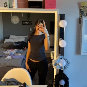 Mörkgrå topp - Säljer en stilren mörkgrå topp med korta ärmar. Perfekt för en avslappnad look. Toppen har en enkel design och är lätt att matcha med olika outfits.