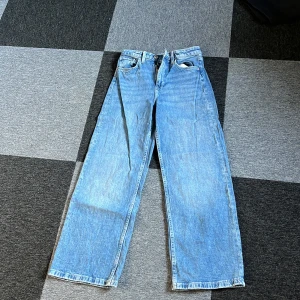 Blå jeans med vida ben från H&M - Säljer ett par snygga blå jeans från H&M med vida ben och hög midja. De har en justerbar midja och stängs med dragkedja och knapp. Perfekta för en avslappnad stil.