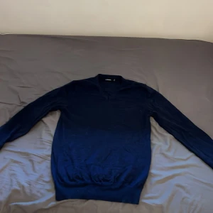 Mörkblå tröja från J.Lindeberg - Säljer en stilren mörkblå tröja från J.Lindeberg. Tröjan har en klassisk design med långa ärmar. Perfekt för en elegant och avslappnad look. Tillverkad i ett mjukt material som känns skönt mot huden.