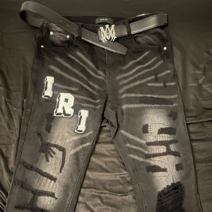 Svarta Amiri jeans  - Snygga svarta jeans från Amiri med unika patchar och slitna detaljer. Byxorna har en cool design med broderade bokstäver och en modern look. Perfekta för dig som vill sticka ut!