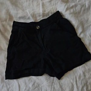 Svarta shorts med knapp - Snygga svarta shorts med knapp och elastisk midja. Perfekta för en avslappnad stil. De har en klassisk design som passar till många olika tillfällen.