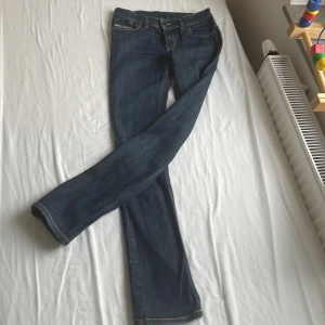 Blå jeans från Diesel - Snygga blå jeans från Diesel med klassisk femficksdesign och kontrastsömmar. Jeansen har en liten logga på myntfickan och är tillverkade i en bomullsblandning för extra komfort. Perfekta för en avslappnad stil.