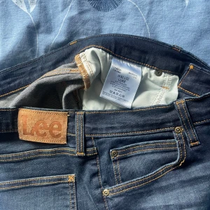 Mörkblå jeans från Lee - Snygga mörkblå jeans från Lee med klassisk femficksdesign och kontrastsömmar. Jeansen har en normal passform och är perfekta för en avslappnad stil. Märkeslogga på baksidan av midjan. Ny inköpta för 1100 för 4 dagar sedan 