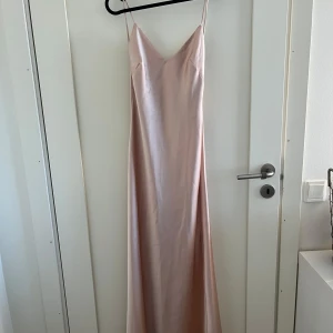 Champagnefärgad rosa balklänning  - Elegant champagnefärgad rosa långklänning med smala axelband och v-ringning. Klänningen har en slät och glansig yta som ger en lyxig känsla. Perfekt för speciella tillfällen. Balklänning i storlek xs från Zara !! Vill meddela att klänningen har en liten fläck längst ner men den syns knappt !! 💘
