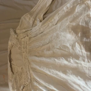 Vit boho-klänning från Gina Tricot - Superfin vit klänning från Gina Tricot med långa ärmar och snygga spetsdetaljer. Klänningen har en luftig känsla och romantiska volanger vid halsen. Perfekt för sommarens alla tillfällen och ger en boho-vibe.