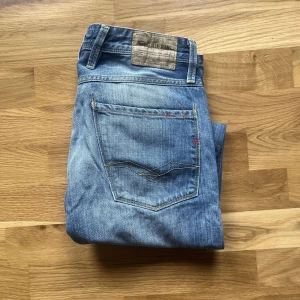 Replay Anbass jeans  - Snygga blå Replay Anbass jeans med klassisk femficksdesign och diskreta slitningar. Jeansen har raka ben och normal passform, tillverkade i slitstarkt denim med coola detaljer på bakfickorna. Perfekta för en avslappnad och trendig look.