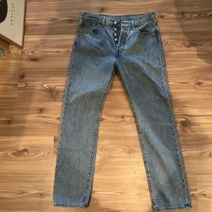Levi's 501 ljusblå jeans W31 L32 - Klassiska Levi's 501 jeans i ljusblå denim med raka ben och knappgylf. Snygg vintagekänsla och ikonisk läderpatch bak i midjan. Perfekta för dig som gillar tidlös stil och vill ha ett par jeans som funkar till allt. Jeansen är i bra skick. Om du vill ha fler bilder eller detaljer så är det bara att höra av sig.