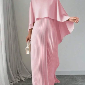 Ljusrosa plisserad långklänning -  ljusrosa långklänning med plisserad kjol och asymmetrisk cape-liknande överdel. Klänningen har en flowy känsla och är perfekt för dig som vill sticka ut med en elegant och modern look. Materialet ser ut att vara mjukt och följsamt, vilket ger en snygg siluett.
