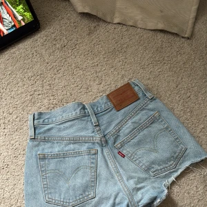 Levi's ljusblå jeansshorts high waist - Säljer ett par ljusblå high waist jeansshorts från Levi's Premium. Klassisk femficksmodell med råa, fransiga kanter och slitningar framtill. Perfekt passform och snygg Levi's-lapp bak. Supersköna och trendiga till sommaren!