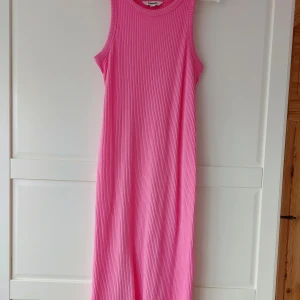 Rosa ribbad långklänning Kappahl - Snygg långklänning från Kappahl i en stark rosa färg. Klänningen är ärmlös med rund halsringning och har en ribbad struktur som ger en cool och modern känsla. Perfekt för varma dagar! Använd max 5 gånger, så nyskick! 