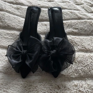 Svarta pumps med stor rosett - Snygga och eleganta svarta pumps med spetsig tå och hög klack. Skorna har en stor, transparent rosett framtill som ger en extra statement-look. 