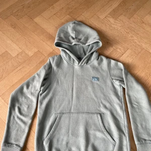 Mintgrön/ turkos hoodie från Jack & Jones - Snygg ljusgrå hoodie från Jack & Jones med broderad logga på bröstet. Tröjan har huva, känguruficka och är tillverkad i mjuk bomullsmix. Perfekt för chill dagar eller när du vill ha en enkel och stilren look.