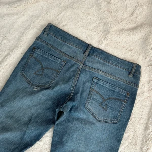Lågmidjade utsvängda jeans - Ett par lågmidjade utsvängda jeans från syb jeans i storlek 40 (L). Jeansen är i bra skick, finns ett hål vid fickan, dock är detta en del av designen. Jag har ingen bild med dom på (för stora). Rakt över midjemått: 39cm. Innebenslängd: 78cm. Total längd: 102cm. Gren: 19cm. Benslut: 23cm. Fast pris D33
