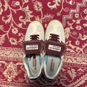 Adidas Wales Bonner  - Unika Adidas Wales Bonner sneakers med beige och bruna detaljer, klassiska tre ränder på sidan och grov stickad sula. Skorna har bruna snören, kontrastsömmar och en cool retrovibe. Materialmix av skinn och textil, med gummisula och tydlig branding på plösen.