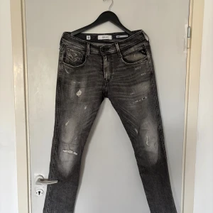 Replay Anbass grå slim jeans - Snygga Replay Anbass jeans i grå tvätt med slitna detaljer och slim fit. Klassisk femficksmodell med svarta och grå nyanser, diskret Replay-logga vid fickan och läderpatch bak. Perfekta för dig som gillar en modern och avslappnad look.