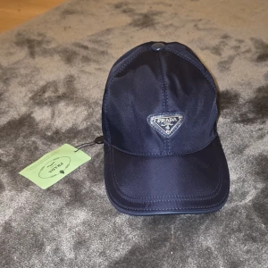 Prada keps - Helt ny Mörkblå prada keps i storlek one size, mycket fin keps i riktigt skön material som passar perfekt för varje klädstil. Går att justera storleken. Pris 400kr.