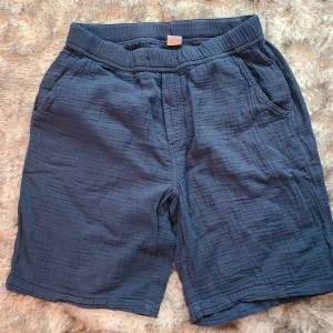 Mörkblå bomullsshorts från Lindex - Mörkblå shorts från Lindex i 100% bomull. De har en avslappnad passform, resår i midjan och praktiska fickor fram och bak. Perfekta för varma dagar och riktigt sköna att ha på sig. Snyggt, enkelt och lättmatchat plagg för sommaren.