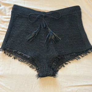 Svarta stickade shorts med fransar - Svarta stickade shorts med snygg snörning i midjan och fransar längs bensluten. De är gjorda i ett stickat material som känns både chill och trendigt. Perfekta för sommarens varma dagar eller som statement-plagg på festival. Helt oanvända med prislapp kvar, säljer då dem var för stora för mig och jag orkade inte skicka tillbaka! 
