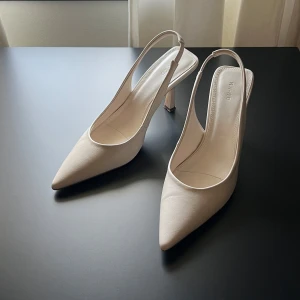 Vita pumps med spetsig tå från NAKD - Stilrena pumps i beige från NAKD med spetsig tå och öppen häl. Skorna har smal klack och är tillverkade i syntetmaterial med en elegant och minimalistisk look. Perfekta för dig som gillar en clean och trendig stil.