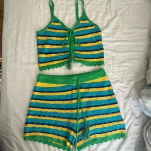 Randig stickad croppad linnetopp och shorts - Matching knit-set for summer. Färgglad stickad linnetopp med gröna axelband och knyt framtill. Toppen har ränder i grönt, gult, blått och svart och en croppad passform. Perfekt för dig som gillar retrovibbar och unika plagg.