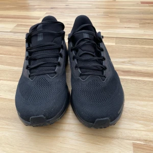 Svarta Nike sneakers Air Zoom storlek 44 - Snygga helsvarta Nike Air Zoom sneakers. Skorna har en sportig vibe med rund tå, platt sula och klassisk snörning. Perfekta för dig som gillar stilrena och bekväma skor till vardags eller träning. Inga täcken på användning och använda endast ett par gånger.