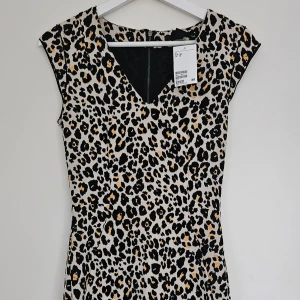 Leopardmönstrad kort klänning - Figurnära leopardmönstrad klänning från H&M med korta ärmar, V-ringad hals & dragkedja bak Storlek: 34 (XS) Ny, aldrig använd - prislapp kvar
