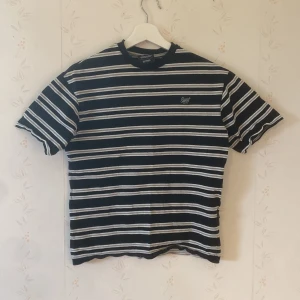 Randig t-shirt från Sweet SKTBS - Svart och vit randig t-shirt från Sweet SKTBS med broderad logga på bröstet. Klassisk passform med korta ärmar och rund hals. Tillverkad i mjuk bomull, perfekt för en chill och stilren look.