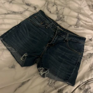 Levi's jeansshorts med råa kanter - Mörkblå jeansshorts från Levi's med klassiska fem fickor och slitna, fransiga benslut. Shortsen har normal passform och tydliga sömmar i kontrastfärg. Perfekta för sommardagar och ger en avslappnad vibe.