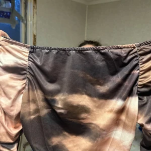 Brun och beige offshoulder topp Shein - Trendig offshoulder topp från Shein i bruna och beige toner med coolt mönster. Långa, rynkade ärmar och croppad passform. Tillverkad i mjuk polyester som sitter skönt och följer kroppen. Perfekt för dig som vill sticka ut med en unik look.