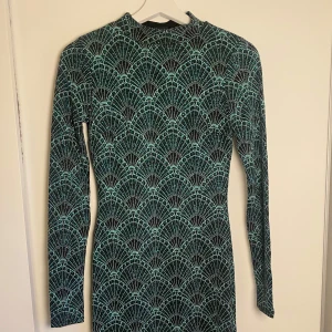 Glittrig långärmad klänning Gina Tricot - Supersnygg långärmad klänning från Gina Tricot med glittrigt mönster i grönt och svart. Tight passform och coolt grafiskt mönster som verkligen sticker ut. Perfekt för dig som vill ha något unikt och trendigt. Materialet är stretchigt och bekvämt.