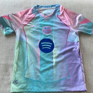 FC Barcelona Lamine Yamal Nike tröja - Säljer en FC Barcelona fotbollströja från Nike med Lamine Yamal och nummer 10 på ryggen. Tröjan har korta ärmar och är i pastelliga färger som blå, rosa, lila och mintgrön. Broderat klubbmärke och Nike-logga, samt Spotify-logga på bröstet. Tillverkad i ventilerande funktionsmaterial.